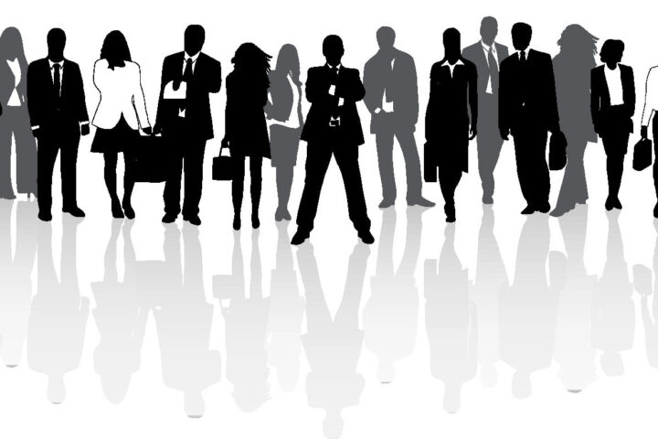 Silhouettes of a group of business people standing together, some holding briefcases, with their reflections visible below them on a white background.