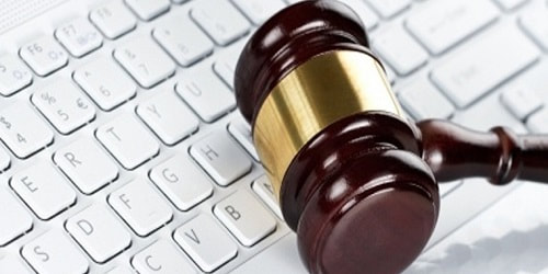A wooden judge’s gavel rests on a computer keyboard, symbolizing digital law or online legal matters.