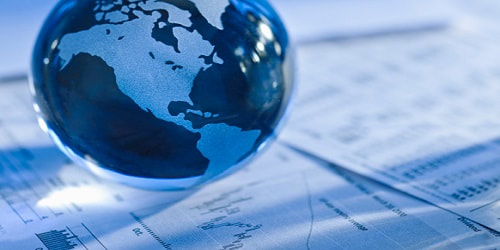 A glass globe showing North and South America sits on top of printed financial charts and graphs.